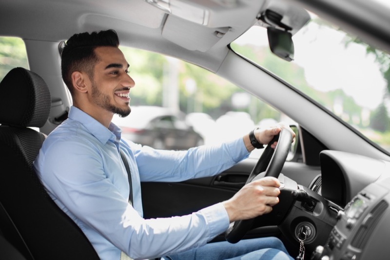 Joyful bearded arabic guy in formal outfit looking at road and smiling